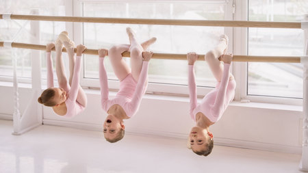 Young ballet students hanging on barre during stretching exercise in studioの写真素材
