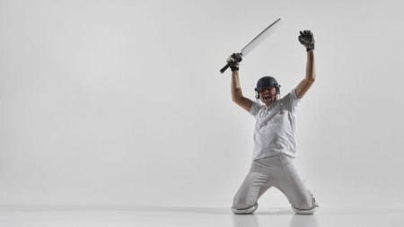 Cricket player celebrating victory on knees with bat raised in studio, shouting with excitement.