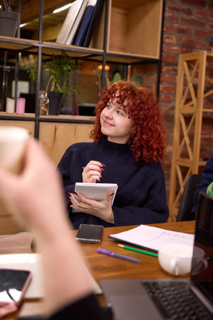 Red haired woman writing notes during office discussion.