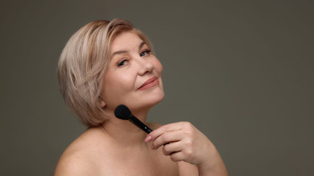 Mature woman posing with makeup brush near chin.の写真素材