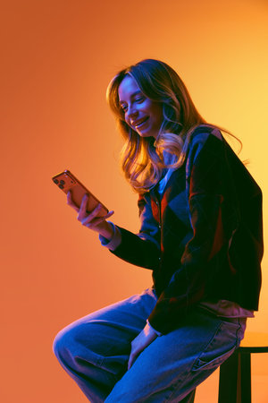 Businesswoman reviewing information on smartphone in studio with vibrant gradient lighting.の写真素材