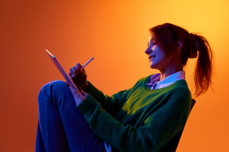 Young woman drawing on tablet with stylus in studio with vibrant gradient lighting