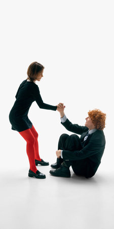 Woman helping seated man stand up holding his hand on white studio background.