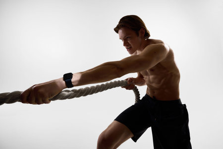 Man training with battle ropes wearing smartwatch in studio.