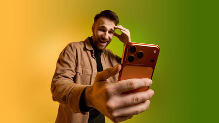 Bearded man reacting to smartphone screen on yellow green gradient background.の写真素材