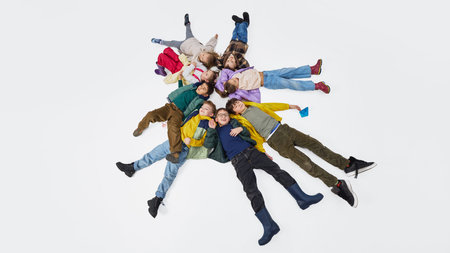 Children lying in circle on floor wearing colorful mid season kids fashion outfits in studio.