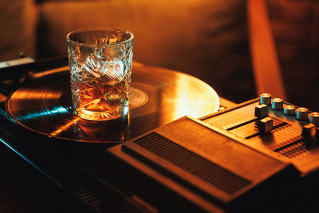 Whiskey drink on turntable beside mixer in warm neon lounge atmosphere.