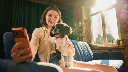 Young woman taking cheerful selfie with small dog in cozy home.