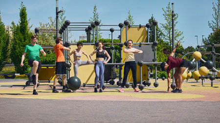 Group of young adults stretching at outdoor fitness park before workout.