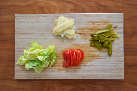 Ingredients For Garnishing a Hamburger Including Tomato Pickles Cheese And Lettuce On  A Chopping Boardの写真素材
