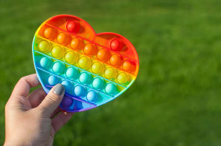 poping up antistress silicone. fidget colorful rainbow toy holding in hand. Sensor new trend on grass backgroundの写真素材
