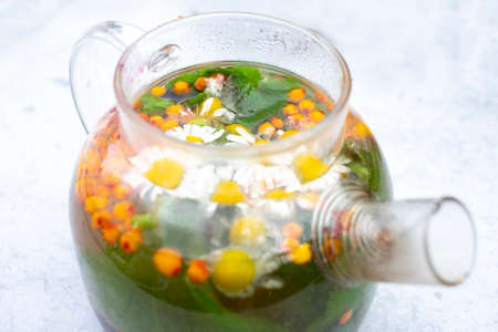 Summer herbal tea with daisy flowers , sea buckthorn and mint leaves in transparent teapot on light...