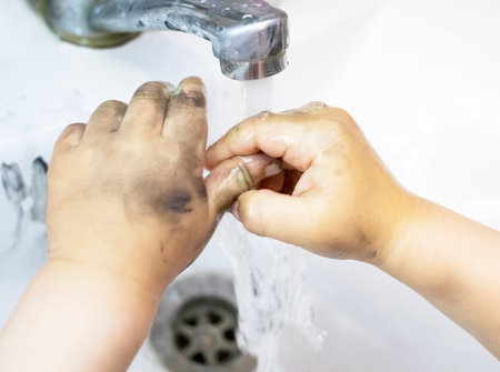 Child washing dirty hands of black paint in bathroomの写真素材