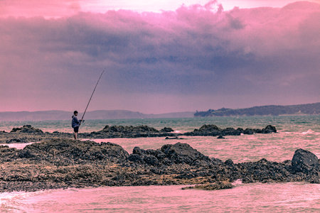 Fisherman with a fishing rod on a rock in the seaの写真素材
