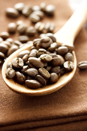 Coffee beans in wooden spoon on brown clothの写真素材