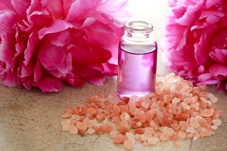 Aroma oil in bottle with pink peony flowers and bath saltの写真素材