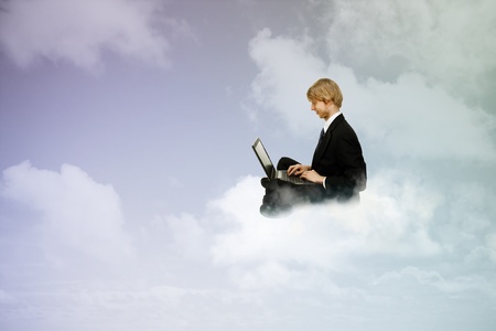 Young business man sitting atop the clouds using a laptop の写真素材