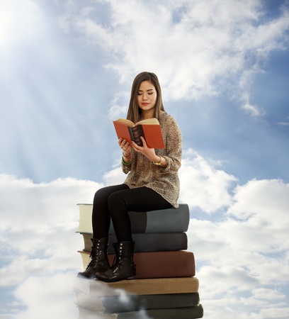 Beautiful Young Woman Reading a Book on Top of Books in the Cloudsの写真素材