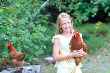 Young Blonde Girl in the Garden caring for Her Chickens in a Yellow Dressの写真素材