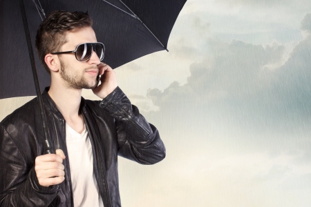Stylish Man Holding an Umbrella and Talking on His Phoneの写真素材