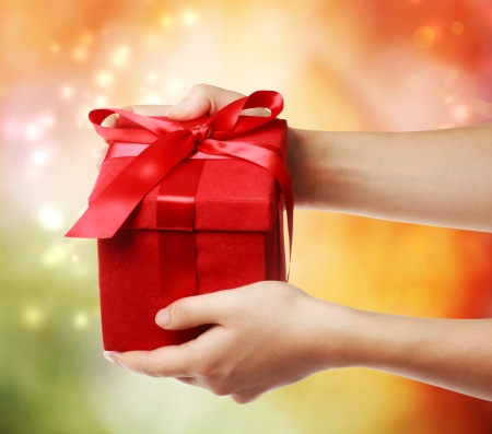 Woman holding a red gift box on a bright holiday lights background の写真素材