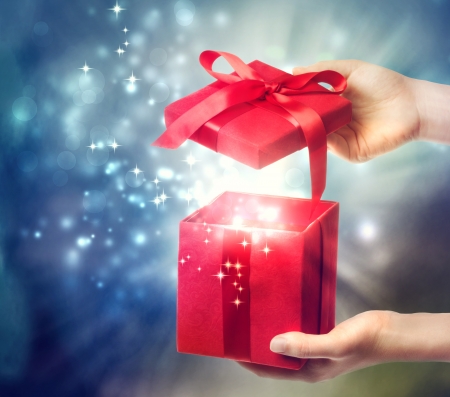 Woman holding a red gift box on a blue holiday lights background の写真素材