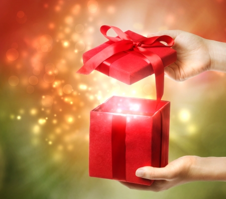 Woman holding a red gift box on a bright holiday lights background の写真素材
