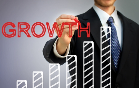 Businessman writing growth over a rising bar graphの写真素材
