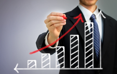 Businessman drawing a rising arrow over a bar graphの写真素材