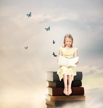 Little Blonde Girl Reading a Book  on Top of Booksの写真素材