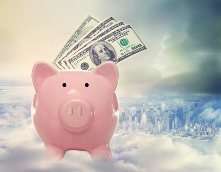 Piggy bank with us dollar bills on a cloud above the cityの写真素材