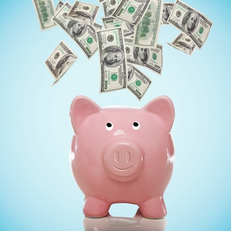 Smiling Piggy bank with hundred dollar bills flowing in or outの写真素材