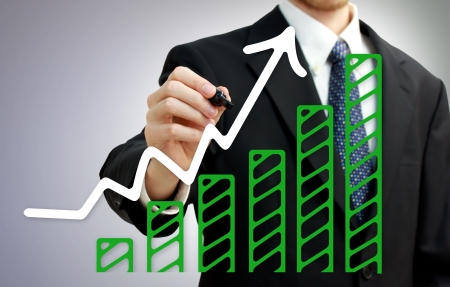 Businessman drawing a rising arrow over growing green bar graphの写真素材