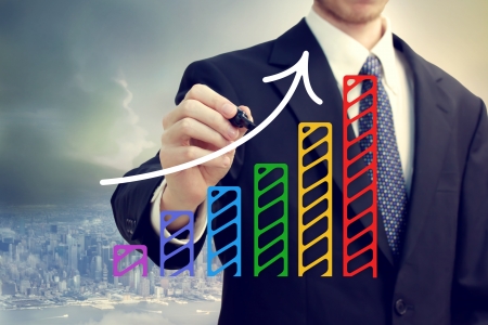 Businessman drawing a rising arrow over a bar graph above the cityの写真素材