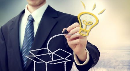 Business man with Idea light bulb coming 'out of the box' with a big city backdropの写真素材
