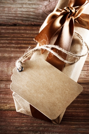 Handmade paper tag with present box with a brown ribbon on a rustic wooden tableの写真素材