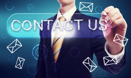 Business Man writing Contact Us in Chalk with Glowing Blue Backgroundの写真素材