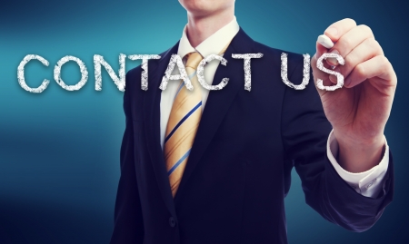 Business Man Writing Contact Us in Chalk with Glowing Blue Backgroundの写真素材