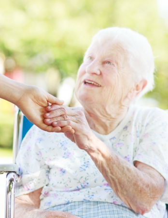 Senior woman in a wheelchair outside holding hands with her caretakerの写真素材
