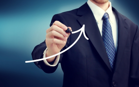 Businessman drawing a rising arrow over blue backgroundの写真素材