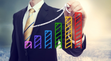Businessman drawing a rising arrow over a bar graph above the cityの写真素材