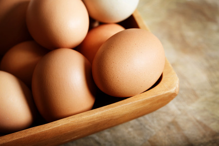 Brown eggs in wooden bowl on wooden tableの写真素材