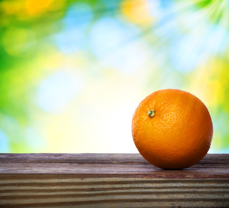 Orange on wooden table over green shiny backgroundの写真素材
