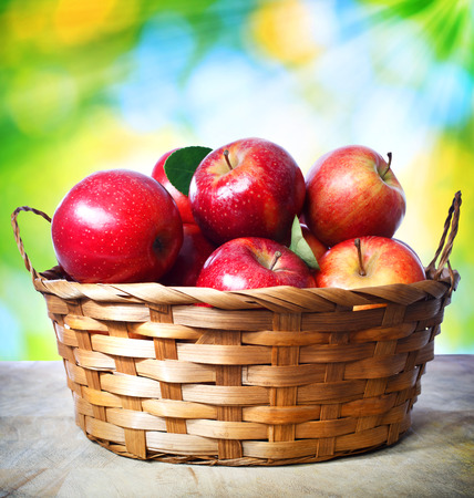 Fresh apples in basket over shiny leaves backgroundの写真素材