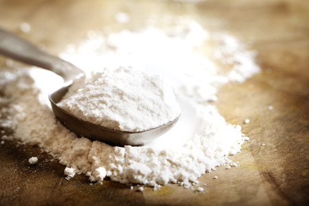 Flour in measuring spoon on rustic wooden boardの写真素材