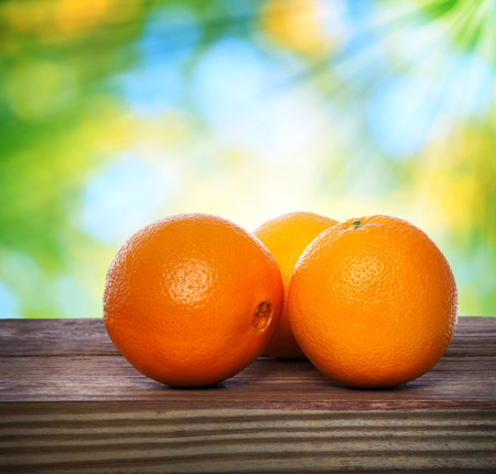 Oranges on wooden table over shiny leaves backgroundの写真素材
