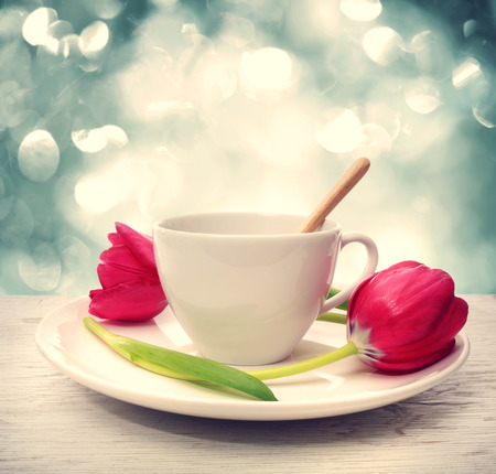 Coffee cup with red tulips over blue shiny backgroundの写真素材