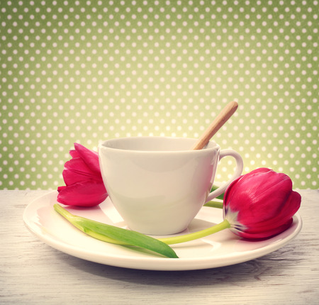 Coffee cup with red tulips over green polka dots backgroundの写真素材