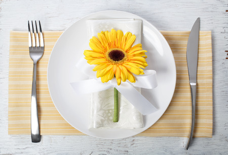 Yellow gerbera with silverware and plate on yellow napkinの写真素材