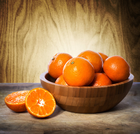 Tangerines in wooden bowl over wooden wall backgroundの写真素材